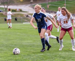 Female soccer player in blue jersey number 39 dribbling the ball during a college match.