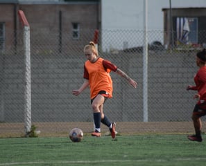 Female soccer player in an orange training vest dribbling the ball during a practice session.