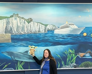 Woman holding little green companion in front of mural of white cliffs of Dover