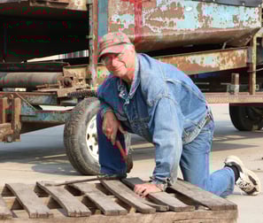 Bob Proctor in work denim, kneeling by a pallet on the ground outside at Poplar Bluff Organics