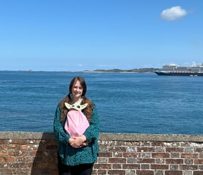 Woman standing in front of low wall with cruise ship in background