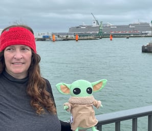 Woman holding little green companion standing at bridge with cruise ship in background