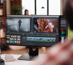 a man sitting at a desk with a computer monitor showing video editing software