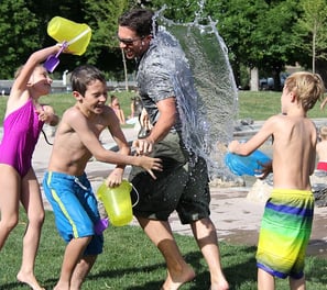 Parent and 3 children having a water fight in the garden on a sunny day