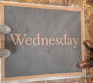 Two pairs of feet around a rug that says "Wednesday"