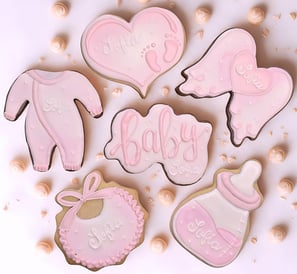 Baby shower themed cookies featuring baby essentials like a baby bottle, onesie, bib, and a cookie with the word baby