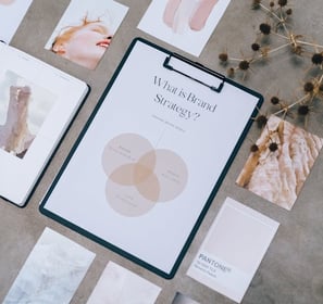 A clipboard titled "What is Brand Strategy?" surrounded by various aesthetic images on a concrete surface.