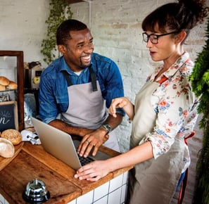 Two small business owners standing behind a counter serving baked goods to customers