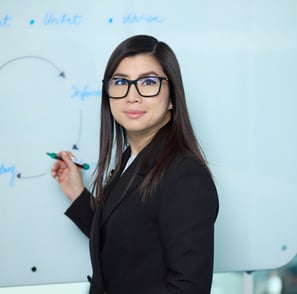 a woman in a suit and glasses is standing in front of a white board