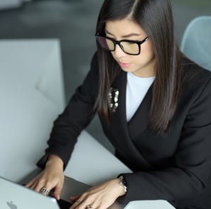 a woman in a suit and glasses is typing on a laptop