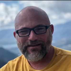 a man with a beard and glasses on a mountain