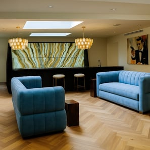 Blue tufted sofas in a stylish lounge with skylight, onyx bar, pendant lights, and James Bond art.