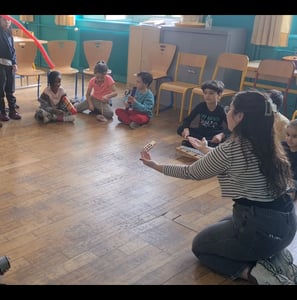 une institutrice dirige ses élèves avec des gestes lors d'un jeu de chef d'orchestre