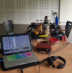 un ordinateur portable avec Ableton Live sur une table avec de nombreux objets sonores et instrument