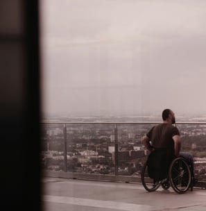 Mann mit Rollstuhl ist auf einem Hotel-Balkon und schaut über eine Stadt