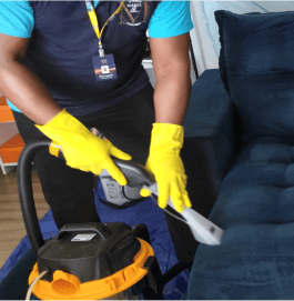 Homem de camisa azul e luvas amarelas limpando um sofá