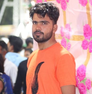 a man in a orange shirt and jeans standing in front of a wall