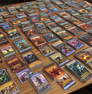 A collection of trading cards from a game called 'Toons and Towers' is spread out on a wooden surface. Each card features a colorful cartoon character and various stats like class, attack, and defense. The characters include a bird, a mushroom, a pig, a chameleon, a cat, and a large bird-like creature.