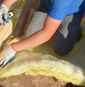 Artisan installant de la laine de verre pour isoler une toiture, garantissant un meilleur confort thermique dans une maison d
