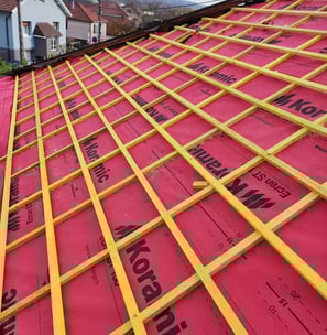 Installation de liteaux et d’un écran de sous-toiture rouge pour préparer la pose des tuiles, sur un chantier de rénovation à
