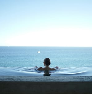 Eine Frau die in einem Infinity Pool auf das Meer schaut
