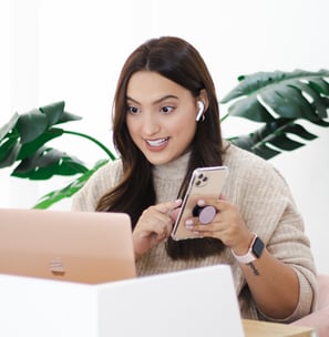 a woman sitting at a table with a cell phone and a laptop