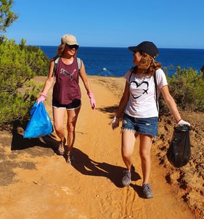 Two female volunteers collecting trash from the sand, cleaning up the beach in Alvor