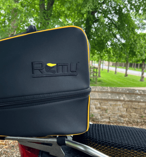 Rider departing on motorcycle with Remy helmet bag secured to the bike, framed against a glowing sun