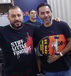 O vocalista da Banda CPM 22 em pé ao lado do ganhador, segurando o skates que ganhou da banda