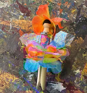 flower fairy clothespin doll laying on a paint-splattered table