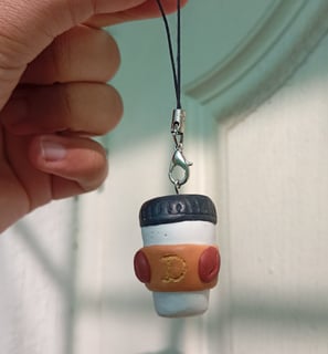 a person holding an engraved white brown coffee cup shaped clay keychain  