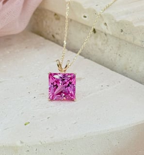 The image showcases a stunning princess-cut pink sapphire pendant necklace, elegantly set in a yello