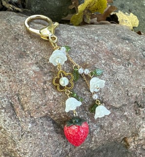 strawberry and flowers key chain with gold tone metal clasp and chain, laying on a rock