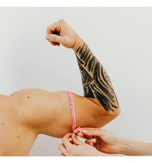 Profissional fazendo medição do bíceps de um homem com uma fita métrica rosa