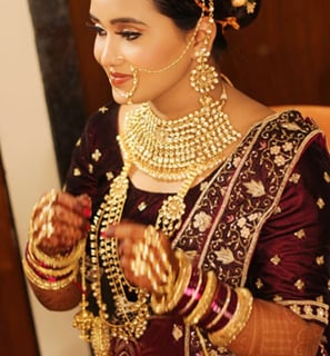 A woman is adorned in traditional bridal attire, featuring intricate jewelry such as a heavy necklac