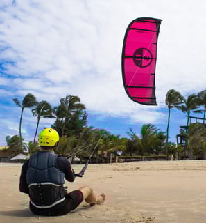 homem controlando o kitesurf sentado na praia