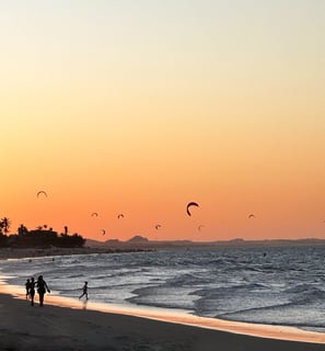 vista da praia do cumbuco no horario do sunset. Varios kites na água e pessoas passeando a beira mar