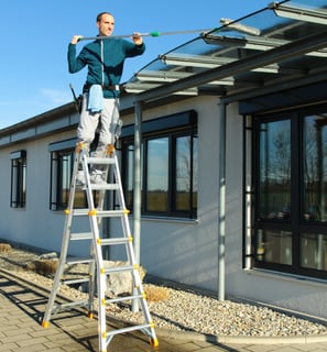 Auf einer Leiter wird mit einer Fensterputzerverlängerung ein Vordach gereinigt. 