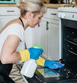 a woman in a white shirt and gloves cleaning a stove