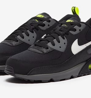 Nike Air Max 90 sneakers in black with neon yellow accents, visible Air cushioning, and mesh upper