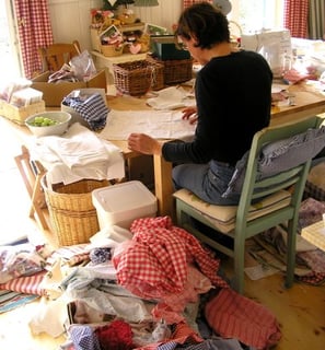 a woman sitting at a table with a lot of clothes on it