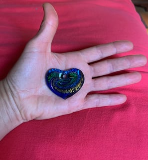 open hand with blue green 7 yellow glass heart on palm