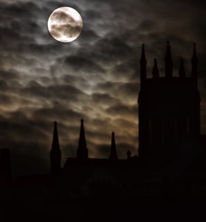 a photo of the moon, partially obscured by clouds, framed by the silhouette of a gothic castle