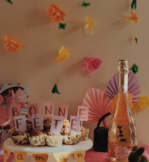 Bonne fête maman sur des muffins avec des fleurs flottantes en arrière plan et une bouteille