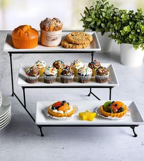 A sleek and modern 3-tier white porcelain plate set with a black metal stand, perfect for serving