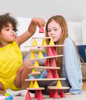 Two children creating a structure from colorful silicone cones and wooden tables in the room