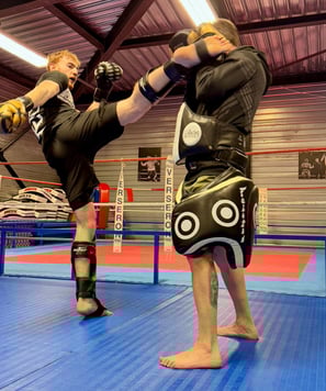Entraînement de boxe : un boxeur en pleine frappe sur une patte d’ours tenue par son coach