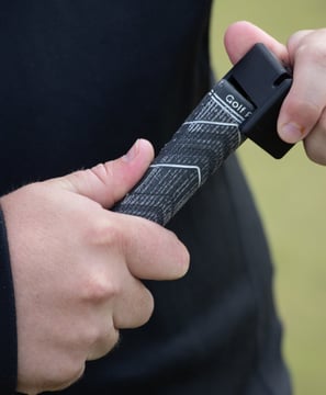 A golfer's hands adjusting a black golf grip tool, Teezup,  on the handle of a club, focusing on the grip and tool in use.