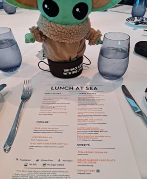 Little Green Companion sitting on table with Lunch menu in front of him