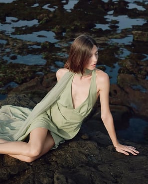 A woman in a sage dress sits on a cliff, captured by Theodorous Yuvens for Asmara Bridal.
